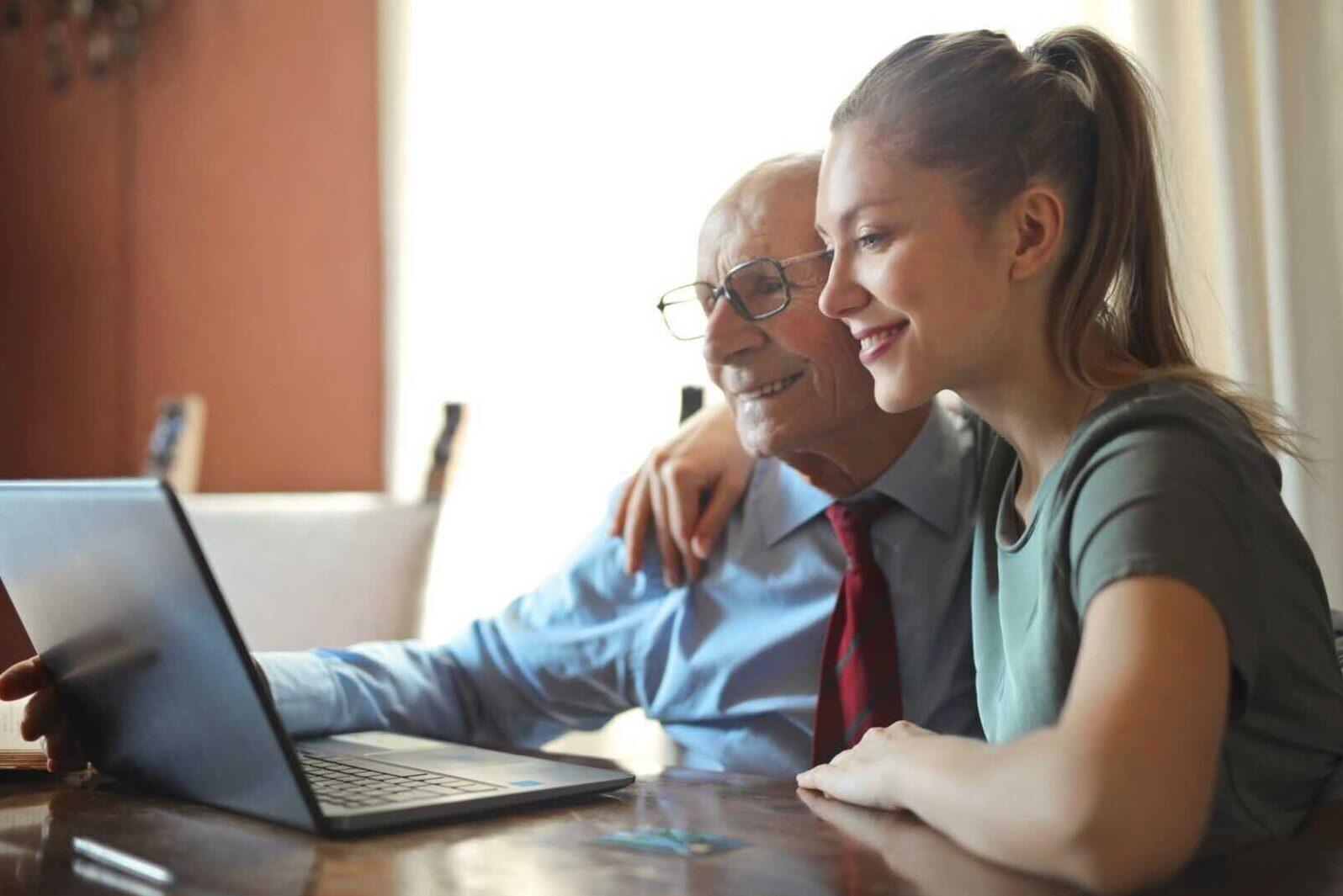 A young woman helping an old man use a laptop