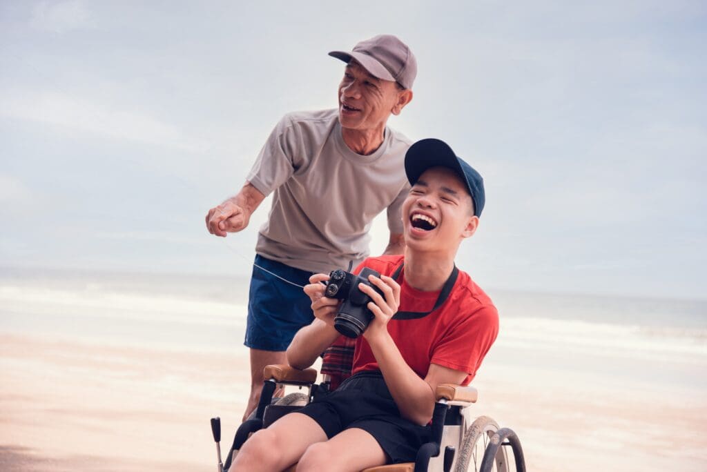 Teenager in a wheelchair on the beach laughing and holding a camera
